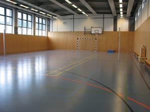 Turnhalle mit grauem Boden, Holzbänken und Fussballtor